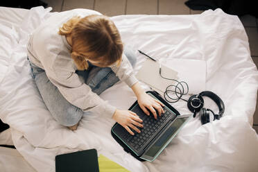 Mädchen macht Hausaufgaben und benutzt einen Laptop im Schlafzimmer zu Hause - MASF24283