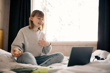 Teenager-Mädchen gestikuliert bei einem Videoanruf während des Hausunterrichts im Schlafzimmer - MASF24284