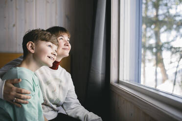 Glückliche Mutter und Sohn sitzen zusammen und schauen durch das Fenster - MASF24286