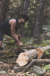 Junger Mann schneidet umgestürzten Baumstamm mit Axt im Wald - JAQF00673