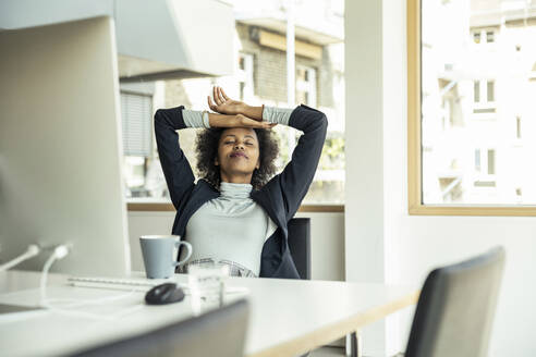 Junge Geschäftsfrau mit Kopf in den Händen entspannt im Büro - UUF23434