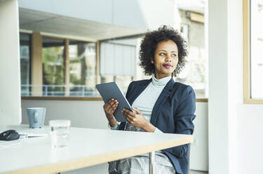 Junge Geschäftsfrau schaut weg und hält ein digitales Tablet im Büro - UUF23440