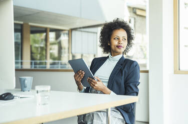 Young businesswoman looking away holding digital tablet at office - UUF23440