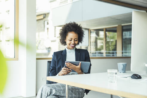 Junge Geschäftsfrau, die ein digitales Tablet benutzt, während sie im Büro sitzt - UUF23442