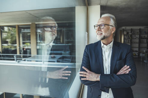 Männlicher Unternehmer schaut durch ein Glasfenster im Büro - UUF23445