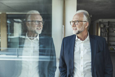 Male professional with eyeglasses looking through glass window at office - UUF23446