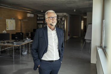 Thoughtful businessman with hands in pockets standing in office - UUF23450