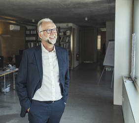 Lächelnder männlicher Berufstätiger, der im Büro steht und wegschaut - UUF23451