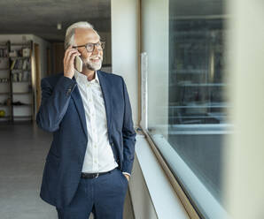 Male entrepreneur with hand in pocket talking on smart phone at office - UUF23454