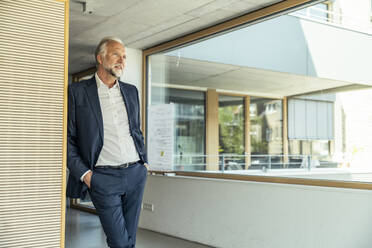 Nachdenklicher Geschäftsmann mit Händen in den Taschen, der sich im Büro anlehnt - UUF23457