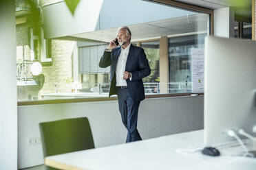 Businessman talking on smart phone while walking in office - UUF23463