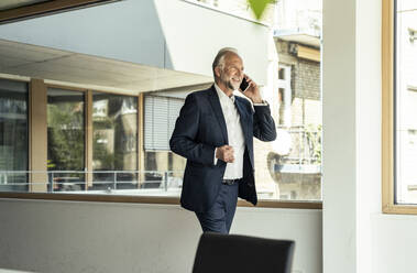 Smiling male entrepreneur talking on smart phone in office - UUF23464