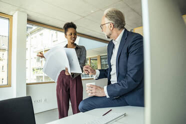 Geschäftsmann im Gespräch mit einer Kollegin, die Dokumente im Büro hält - UUF23471