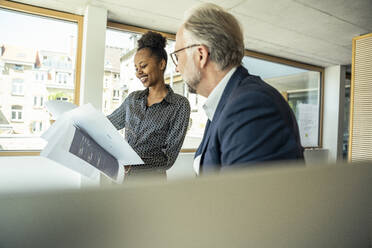 Smiling businesswoman with male colleague looking at strategy in office - UUF23473