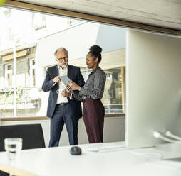 Male professional explaining female colleague over digital tablet in office - UUF23475