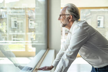 Male entrepreneur leaning near glass window at office - UUF23483