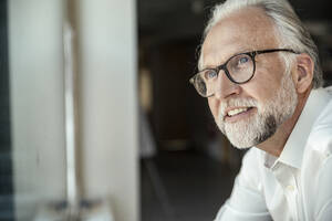 Smiling businessman with eyeglasses day dreaming at office - UUF23485