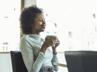 Geschäftsfrau mit Kaffeetasse im Büro sitzend - UUF23514