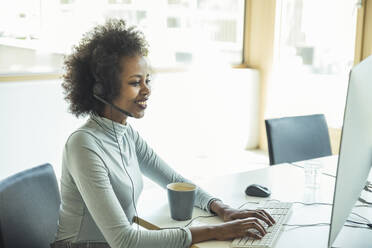 Young female professional wearing headset while using computer at office - UUF23517