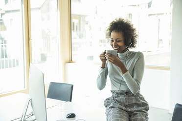 Businesswoman having coffee while looking at computer in office - UUF23520