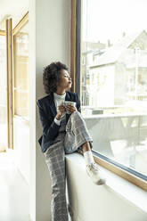 Young businesswoman with eyes closed sitting on window sill at office - UUF23528