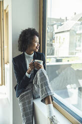 Smiling businesswoman day dreaming while sitting on window sill at office - UUF23529