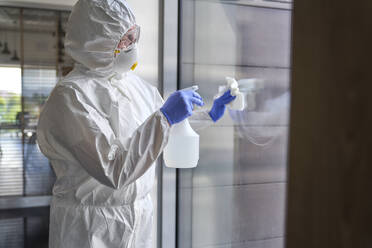 Weibliche Reinigungskraft sprüht bei der Desinfektion eines Bürogebäudes Chemikalien auf Glas - ABIF01368