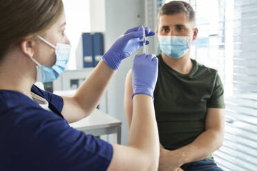 Female healthcare worker preparing vaccine syringe for male patient at center - ABIF01392