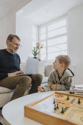 Son looking at father working on laptop at home - MFF07978