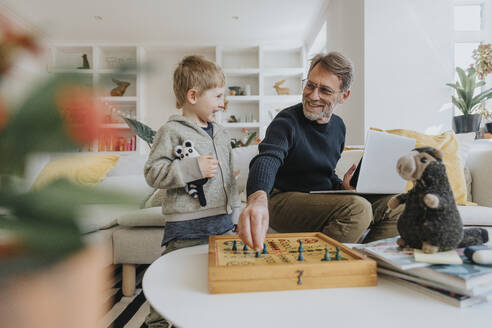 Happy father playing ludo game with son at home - MFF07980