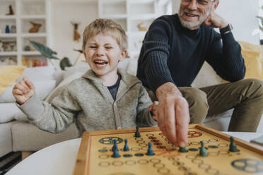 Fröhlicher Sohn spielt Ludo mit seinem Vater zu Hause - MFF07984