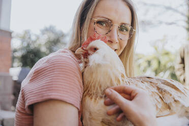 Mittlere erwachsene Frau lächelt, während sie ein Huhn umarmt - MFF08011