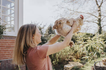 Mittlere erwachsene Frau, die ein Huhn im Hinterhof aufliest - MFF08013