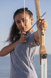 Young woman practicing archery with bow and arrow - JRVF00966
