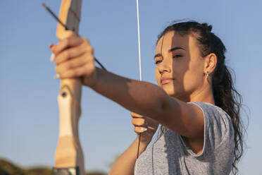 Young woman aiming with bow and arrow during sunny day - JRVF00970