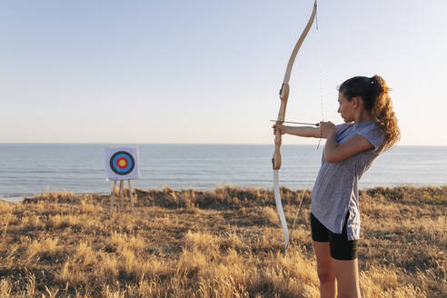 Archeress aiming at target while standing on grass during sunny day - JRVF00977