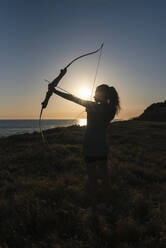 Junge Frau hält Pfeil und Bogen bei Sonnenuntergang - JRVF00978
