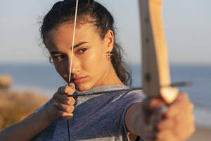 Konzentrierte junge Frau übt Bogenschießen mit Pfeil und Bogen - JRVF00980