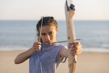 Junge Frau übt Bogenschießen am Strand - JRVF00984