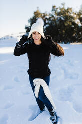 Smiling woman wearing knit hat enjoying in snow - MRRF01238