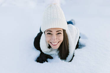 Glückliche Frau mit Strickmütze auf Schnee liegend - MRRF01241