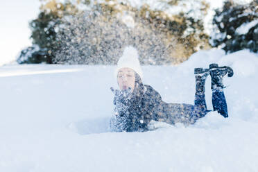 Playful woman blowing snow while lying down - MRRF01244