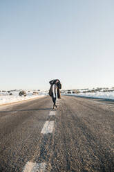Mid adult woman standing on empty road during winter - MRRF01253