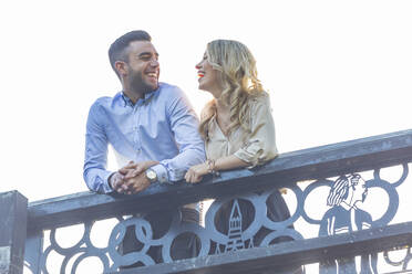 Cheerful couple looking at each other while leaning on railing - WPEF04712