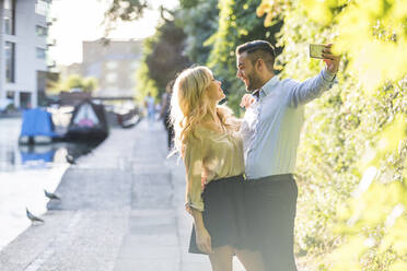 Happy couple looking at each other while taking selfie through smart phone - WPEF04716