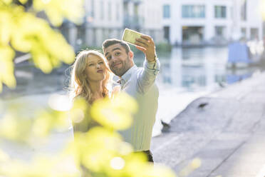 Young woman puckering while taking selfie with boyfriend through smart phone - WPEF04717