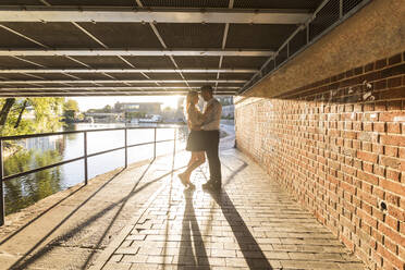 Romantic couple standing on footpath below bridge during sunset - WPEF04723