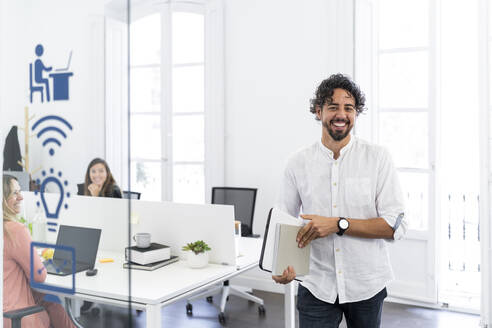Lächelnder männlicher Unternehmer, der nach einer Besprechung aus einer Bürozelle geht - MPPF01847