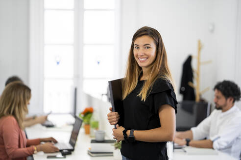 Businesswoman holding documents while standing in coworking office - MPPF01849