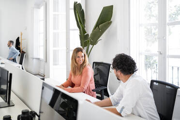 Lächelnde Unternehmerin, die einen männlichen Mitarbeiter ansieht, während sie im Büro sitzt - MPPF01853